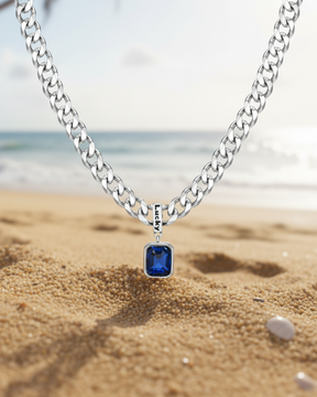 Colar masculino prateado modelo Irsina com pedra de zircônia azul escuro Classiatti com fundo de uma praia
