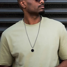Homem usando colar prateado discreto com pingente redondo preto na camiseta.