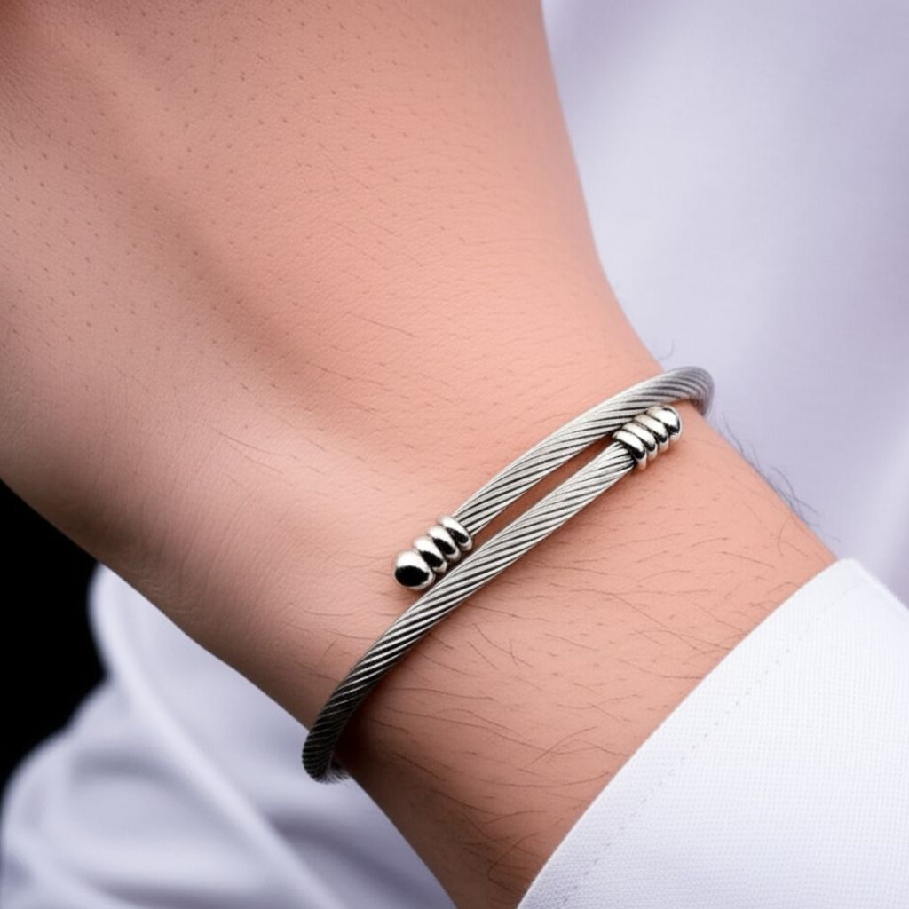 Homem usando bracelete rígido prateado estilo cabo de aço torcido no pulso.
