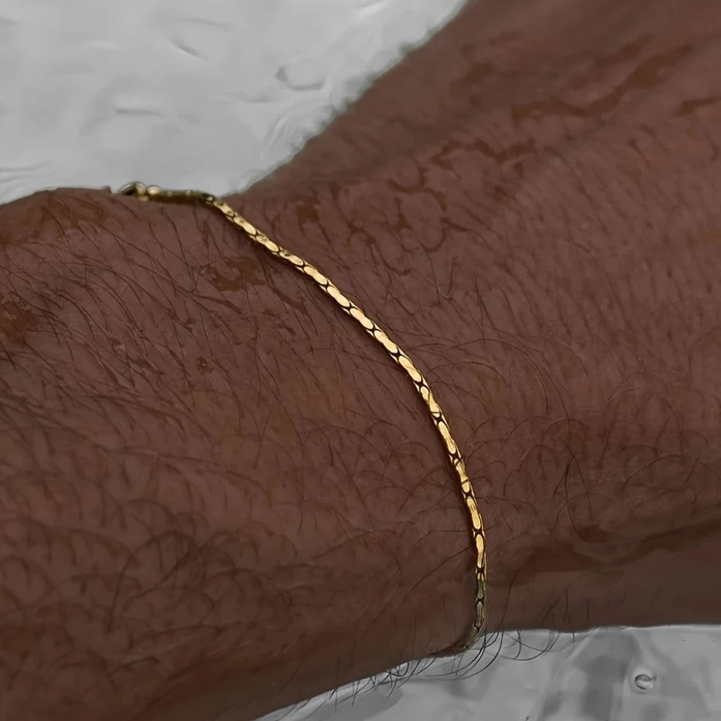 Homem usando pulseira de corrente fina dourada minimalista no pulso.
