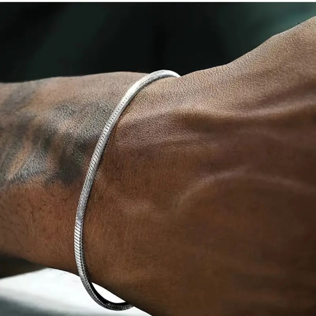 Homem usando pulseira fina de fio redondo prateado (estilo snake) no pulso.