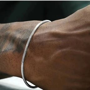 Homem usando pulseira fina de fio redondo prateado (estilo snake) no pulso.